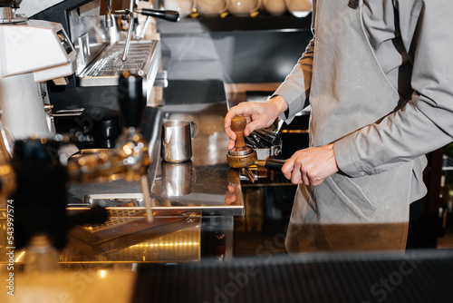 Close-up of a masked bartista preparing delicious delicious coffee at the bar in a coffee shop. The work of restaurants and cafes during the pandemic.