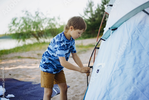 cute little caucasian boy helping to put up a tent. Family camping concept photo