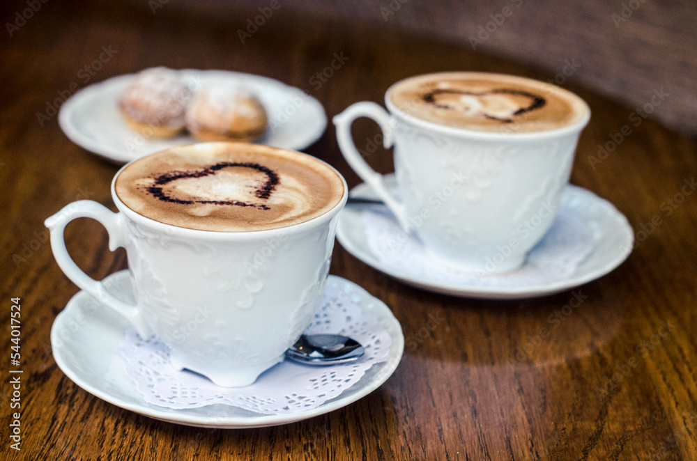 Two cups of coffee with pictures of hearts and a nut cake on a wooden table. Two cups of coffee with pictures of hearts and a nut cake on a wooden table.