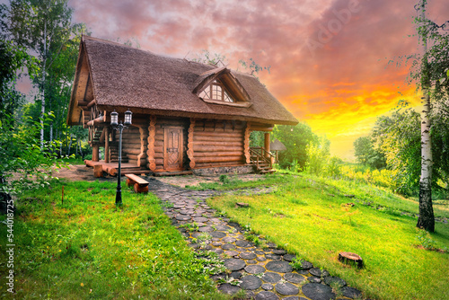 Path and wooden house in birch grove under dramatic sunset skies