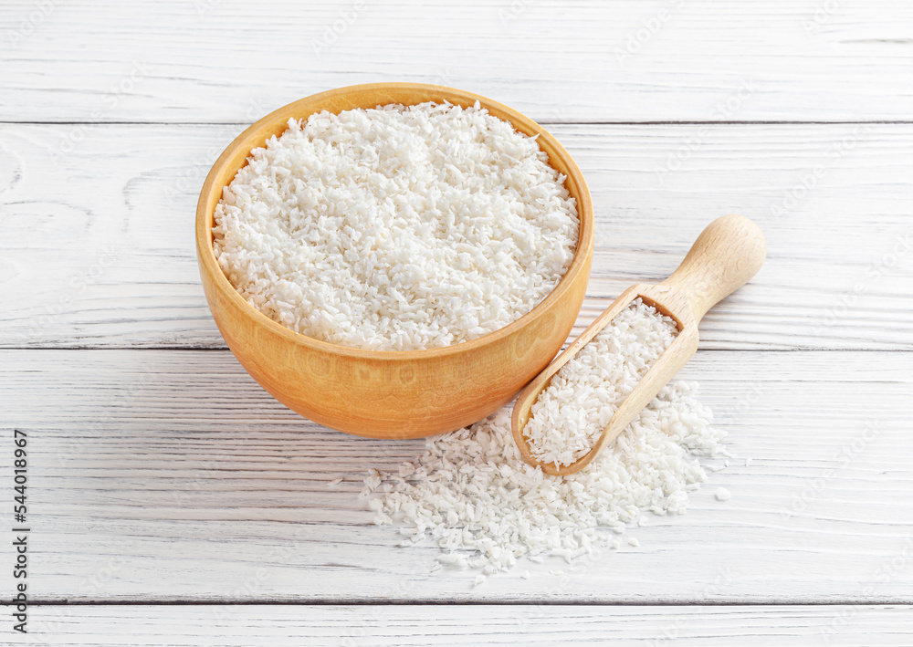 Coconut flakes in wooden bowl with scoop on white wooden background