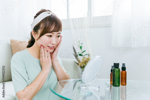 鏡を見ながら化粧品・コスメで保湿する日本人女性
