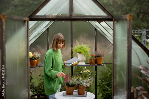 Woman with digital tablet growing plants in greenhouse