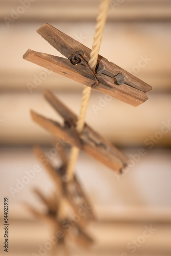 A line of old wooden clothes pegs on a nylon washing line with rusty metal springs make an attractive arrangement against a dark and creamy background