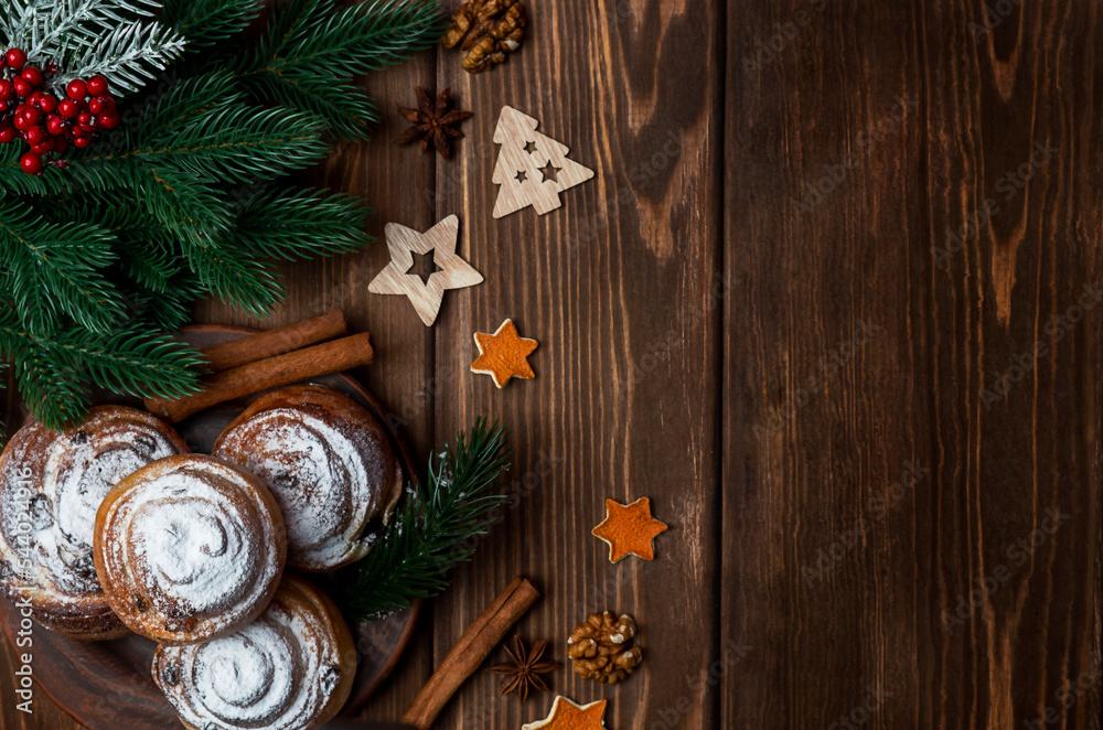 Scones on a plate with cinnamon and walnuts on a wooden background with fir branches, wooden toys and other elements. Top view. New Year Christmas. Scones on a plate with cinnamon and walnuts on a wooden background with fir branches, wooden toys and other elements. Top view. New Year Christmas.