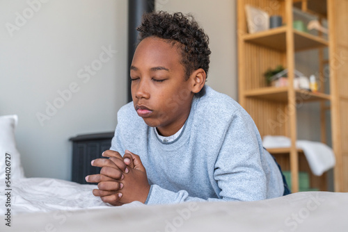 Boy with eyes closed praying by bed at home photo