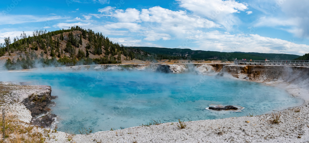 Beautiful panoramic view of smoke emitting from Excelsior geyser. Geothermal landscape and mountains with cloudy sky in background. Famous sightseeing attraction at Yellowstone national park.