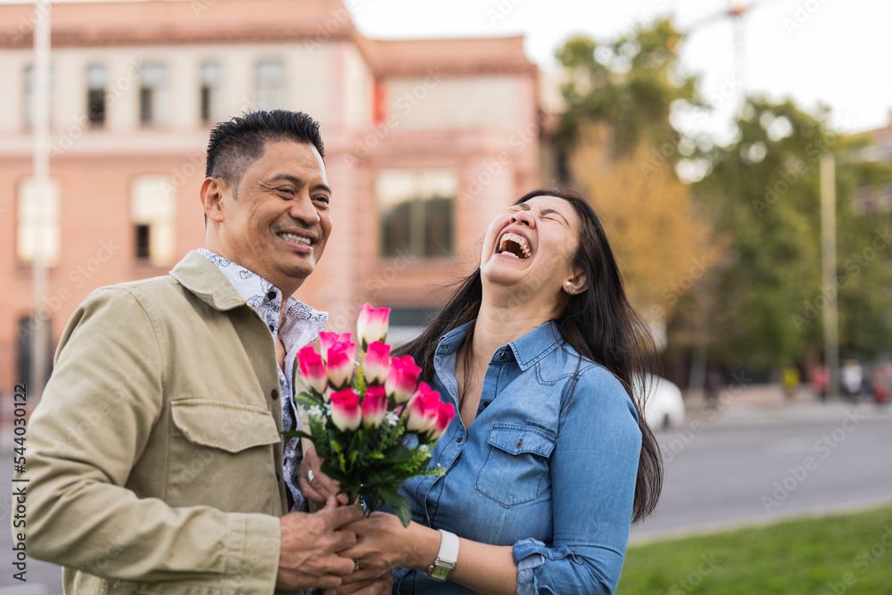 Happy mature couple holding flowers in front of building on Valentine's day Happy mature couple holding flowers in front of building on Valentine's day