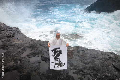 Monk showing calligraphy on paper standing in front of sea