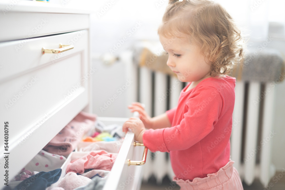 toddler girl arranges clothes and close drawer at home - obrazy, fototapety, plakaty 