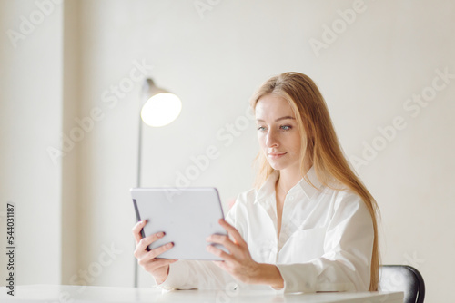 Photo of a cheerful young blonde business woman in office indoors work with laptop and mobile phone.