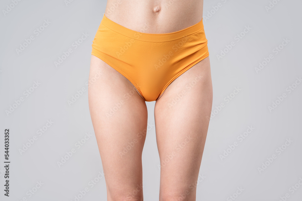 Skinny woman in orange panties on gray background, slim female thighs Stock  Photo