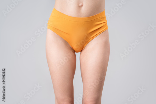 Skinny woman in orange panties on gray background, slim female thighs photo