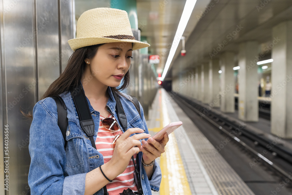 closeup of asian girl wearing hat checking timetable on her mobile phone on the platform of Osaka underground in japan