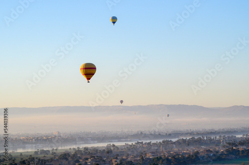 Colorful hot air balloons fly over the green field at sunrise in Valley of the Kings and red cliffs western bank of the Nile river- Luxor- Egypt