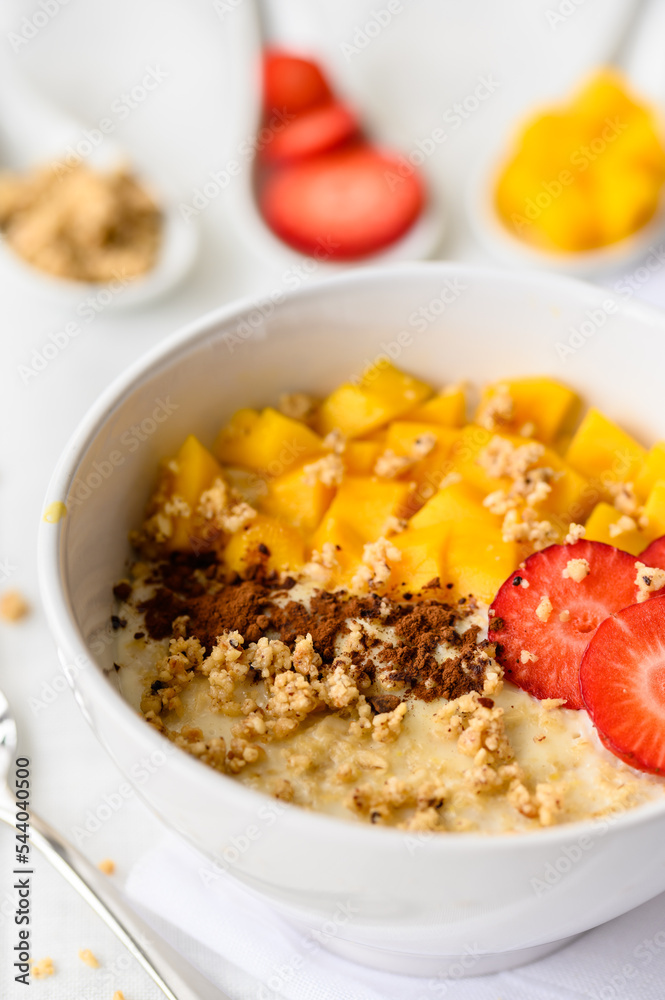 Close up view oatmeal porridge with strawberries, mango and nuts