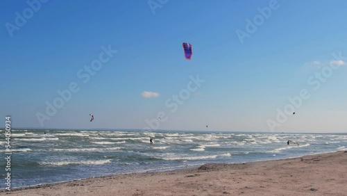 A man in a wetsuit on a parachute rides a board on the waves of the sea. A young man performs a trick in the air against the sky. Water sports, kitesurfing, paragliding, hydrofoil, surfing photo