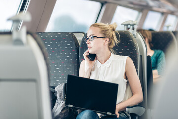 Businesswoman talking on cellphone and working on laptop while traveling by train. Business travel concept.