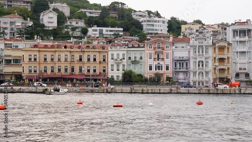 ISTANBUL - AUGUST 06, 2021: Beautiful colorful old houses at Bosporus waterfront, view of Arnavutkoy from moving ferryboat. Old area of Istanbul city, new houses seen on green hill at background photo