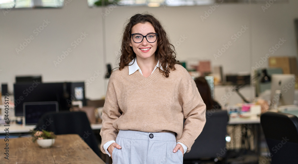 Young happy smiling pretty professional business woman at workplace, female  company office worker, entrepreneur or businesswoman executive standing in  office, looking at camera, portrait. Stock Photo