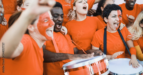 Multiracial orange sport fans screaming while supporting their team - Football supporters having fun at competition event - Focus on african man face