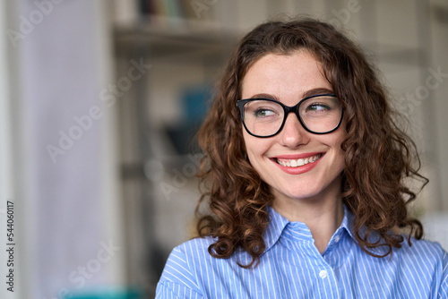 Young smiling interested professional business woman, happy female office worker wearing eyeglasses looking away at copy space advertising new career opportunities or good business services.