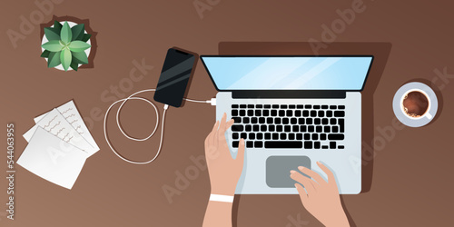 Desktop view from above, a girl works at a laptop, charges her phone, documents lie nearby coffee and succulent are standing