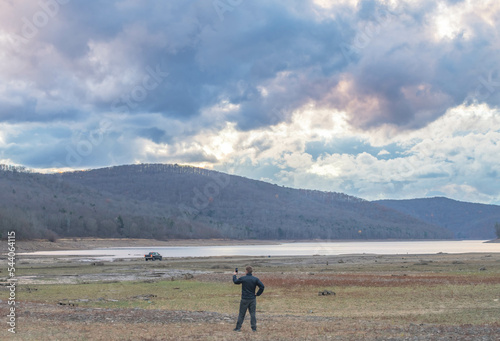 Man taking a selfie with his phone on a waters age lake mountain landscape