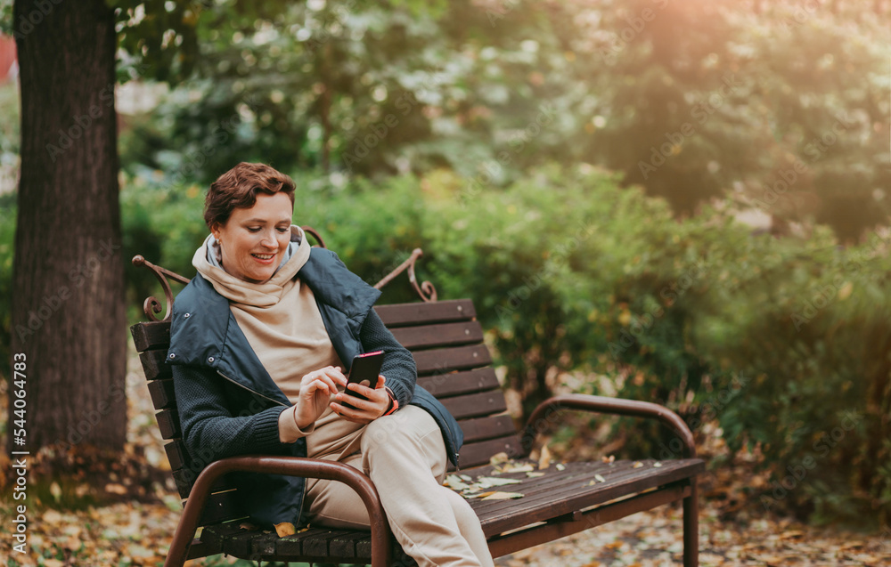 Fototapeta premium A woman in an autumn park reads messages in a smartphone