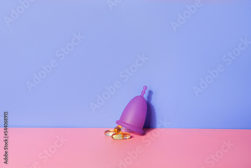 Female menstual cup and oil capsules on pink table. Woman well-being concept photo