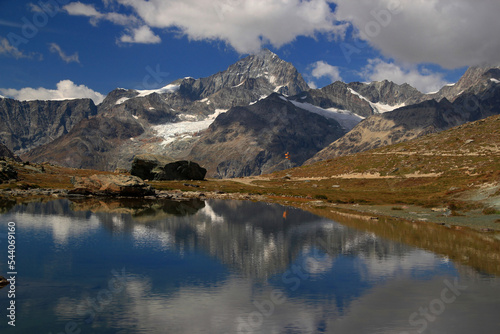 A landscape with a smooth lake surface and mountains and clouds reflected in it, on a mountain Gornergrat, near Zermatt, in southern Switzerland