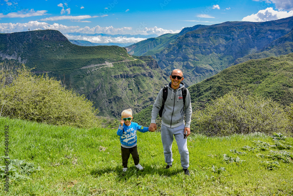 A man with a child on the background of a mountain view from the territory of the Tatev monastery, an Armenian Apostolic monastery of the 9th century, Armenia. May 5, 2019.