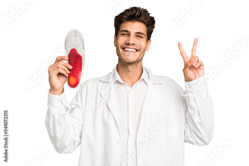 Young caucasian chiropodist man isolated joyful and carefree showing a peace symbol with fingers.