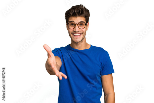 Young caucasian handsome man isolated stretching hand at camera in greeting gesture.