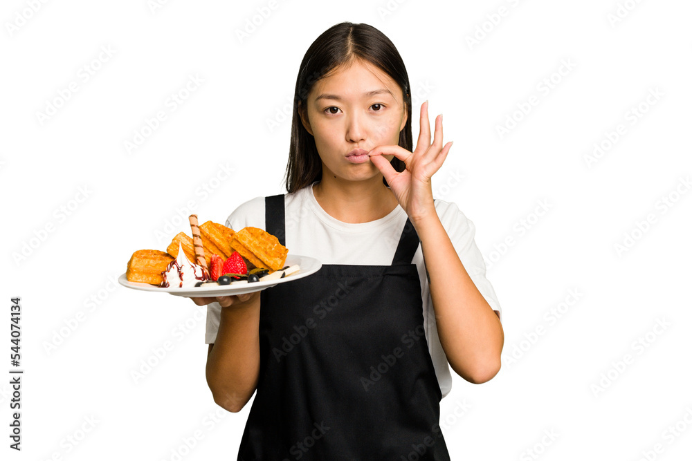 Young asian waitress woman holding waffles isolated with fingers on lips keeping a secret. Young asian waitress woman holding waffles isolated with fingers on lips keeping a secret.