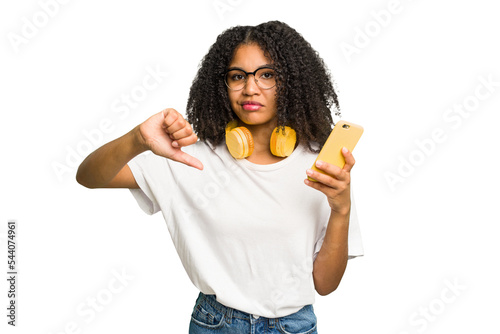 Young african american woman listening to music with yellow headphones isolated showing a dislike gesture, thumbs down. Disagreement concept.