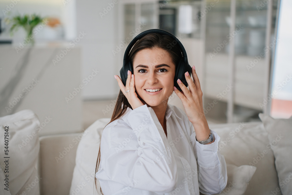 Close up portrait of brunette Hispanic woman in headphones and white shirt toothy smiling sitting on cozy sofa at home. Domestic leisure activities. Beautiful student girl realaxing home. Close up portrait of brunette Hispanic woman in headphones and white shirt toothy smiling sitting on cozy sofa at home. Domestic leisure activities. Beautiful student girl realaxing home.