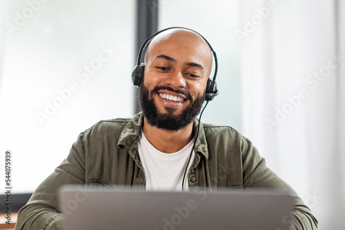 Happy latin man with beard in headphones looking at laptop and smiling, having video call from home