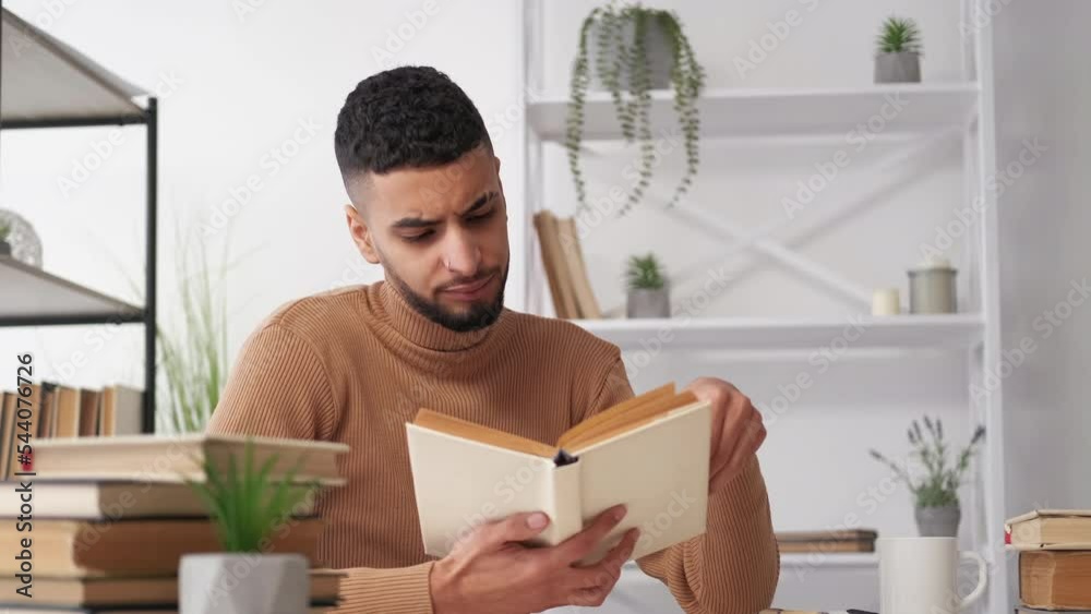 Hard education. Male student. Exhausted study. Tired casual man sitting desk reading book yawning in light room interior.