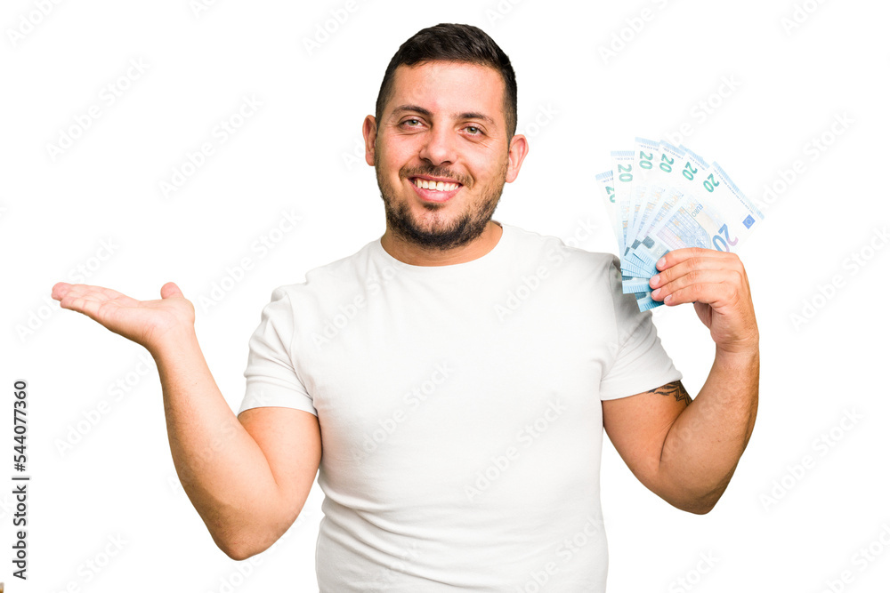 Young caucasian man holding a banknotes isolated showing a copy space on a palm and holding another hand on waist. Young caucasian man holding a banknotes isolated showing a copy space on a palm and holding another hand on waist.