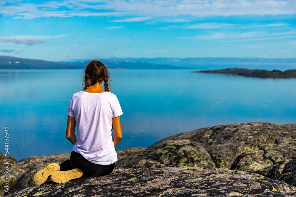girl sits on rocks admiring the sunrise over a bay in northern norway; hiking in nordic norway, rugged landscape of the norwegian fjords girl sits on rocks admiring the sunrise over a bay in northern norway; hiking in nordic norway, rugged landscape of the norwegian fjords