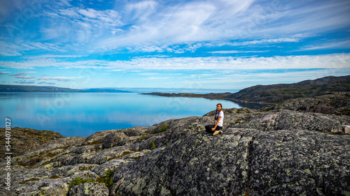 girl sits on rocks admiring the sunrise over a bay in northern norway; hiking in nordic norway, rugged landscape of the norwegian fjords