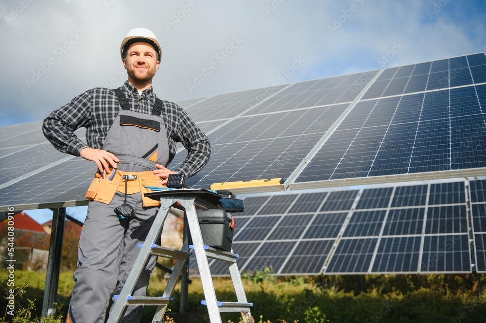 Portrait of smiling confident engineer technician with electrical screwdriver, standing in front of unfinished high exterior solar panel photo voltaic system Portrait of smiling confident engineer technician with electrical screwdriver, standing in front of unfinished high exterior solar panel photo voltaic system