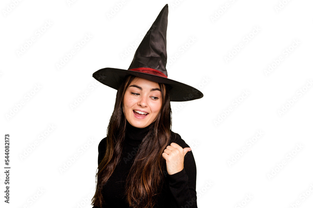 Young caucasian woman dressed as a witch isolated on green chroma background points with thumb finger away, laughing and carefree. Young caucasian woman dressed as a witch isolated on green chroma background points with thumb finger away, laughing and carefree.