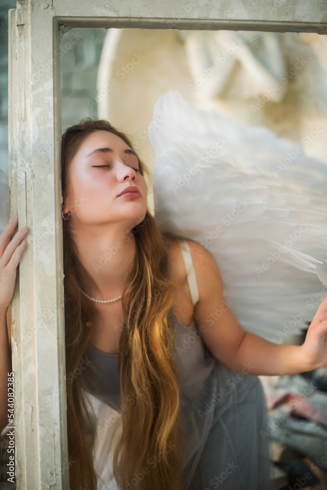 Fototapeta premium Time to go beyond. An angel girl with long hair holds a white frame and looks away. Portrait