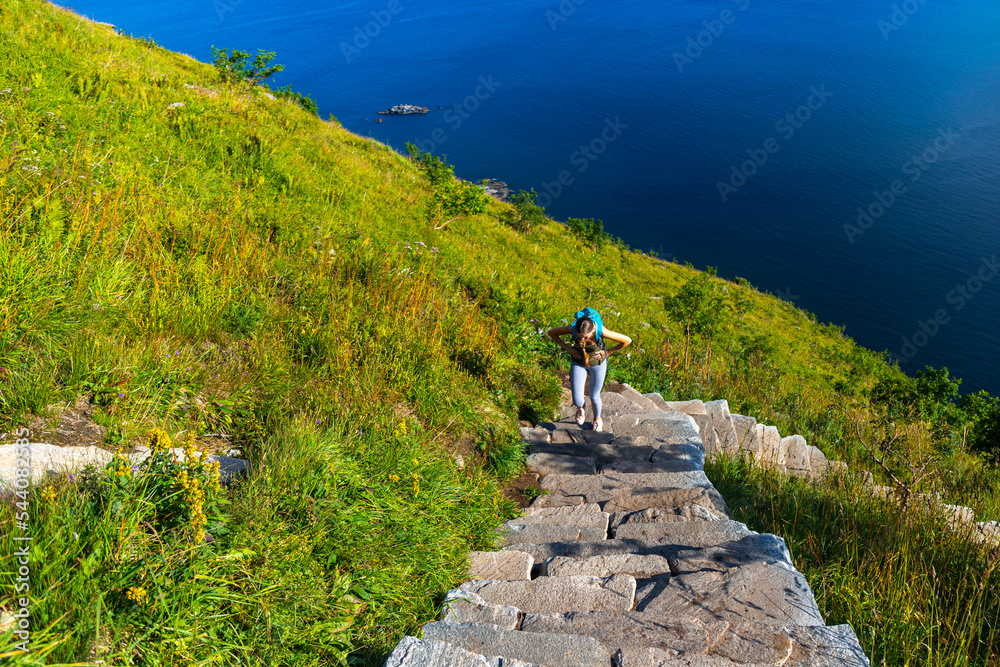 girl backpacker hiking up stairs to famous reinebringen peak in lofoten islands, norway; challenging stair climbing; hiking in lofoten islands