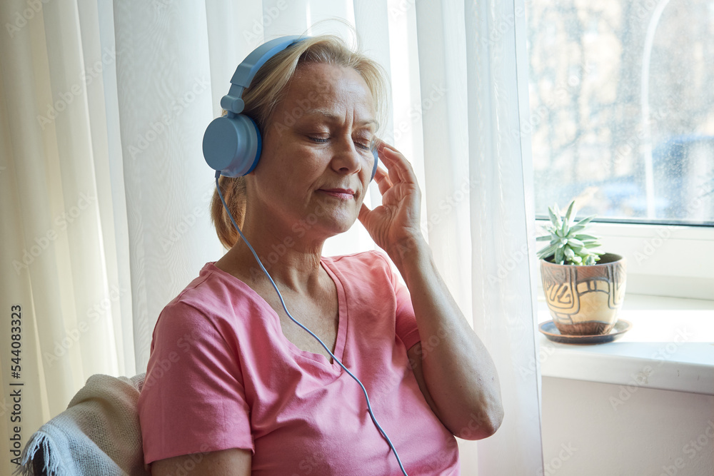 Naklejka premium Close up senior woman in blue headphones enjoying music with her eyes closed