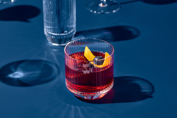 Popular cocktail negroni with gin and vermouth on blue background with shadow. Negroni cocktail on coloured background in trendy style. Contemporary concept with alcohol beverage. Bartender cocktail.