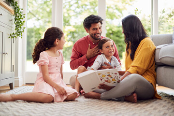 Family At Home Sitting On Floor In Lounge Reading Book Together