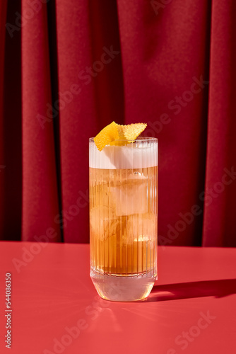 Classic cocktail whiskey sour with egg foam in highball glass on red background. Whiskey sour on coloured background in trendy style. Contemporary concept with alcohol beverage with shadow.